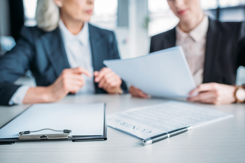 Cropped view of two businesswomen discussing business project on meeting in office, clipboard and contract on foreground